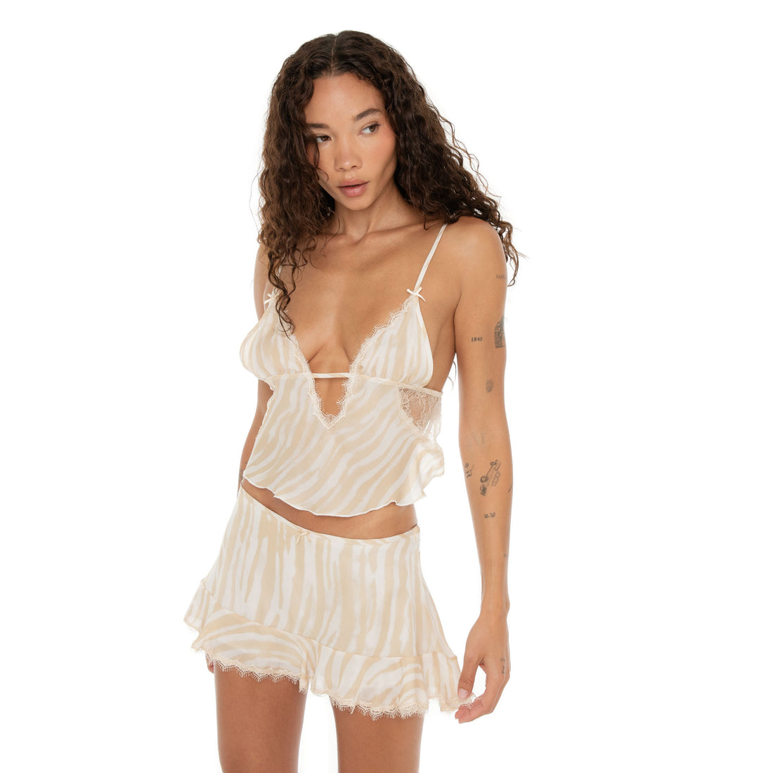 Model in Aria Skirt and camisole in ivory latte looking to the side with one arm bent, showing off the skirt’s ruffled hem.**ivory-latte