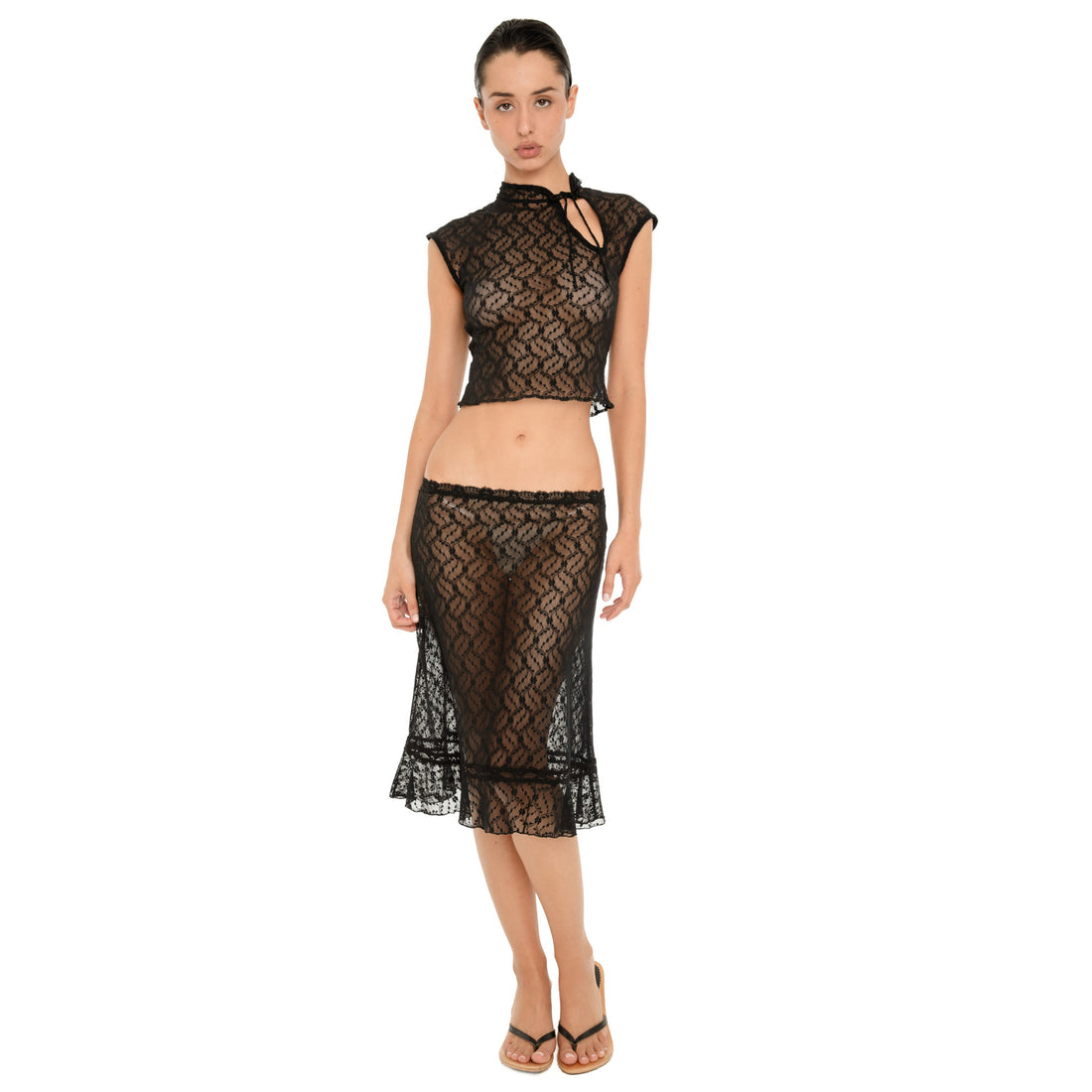 Full-length front view of a model wearing the sheer black floral lace Liulu Skirt, showing the low-rise fit, fitted silhouette, lace waistband trim, and ruffled hem. **black