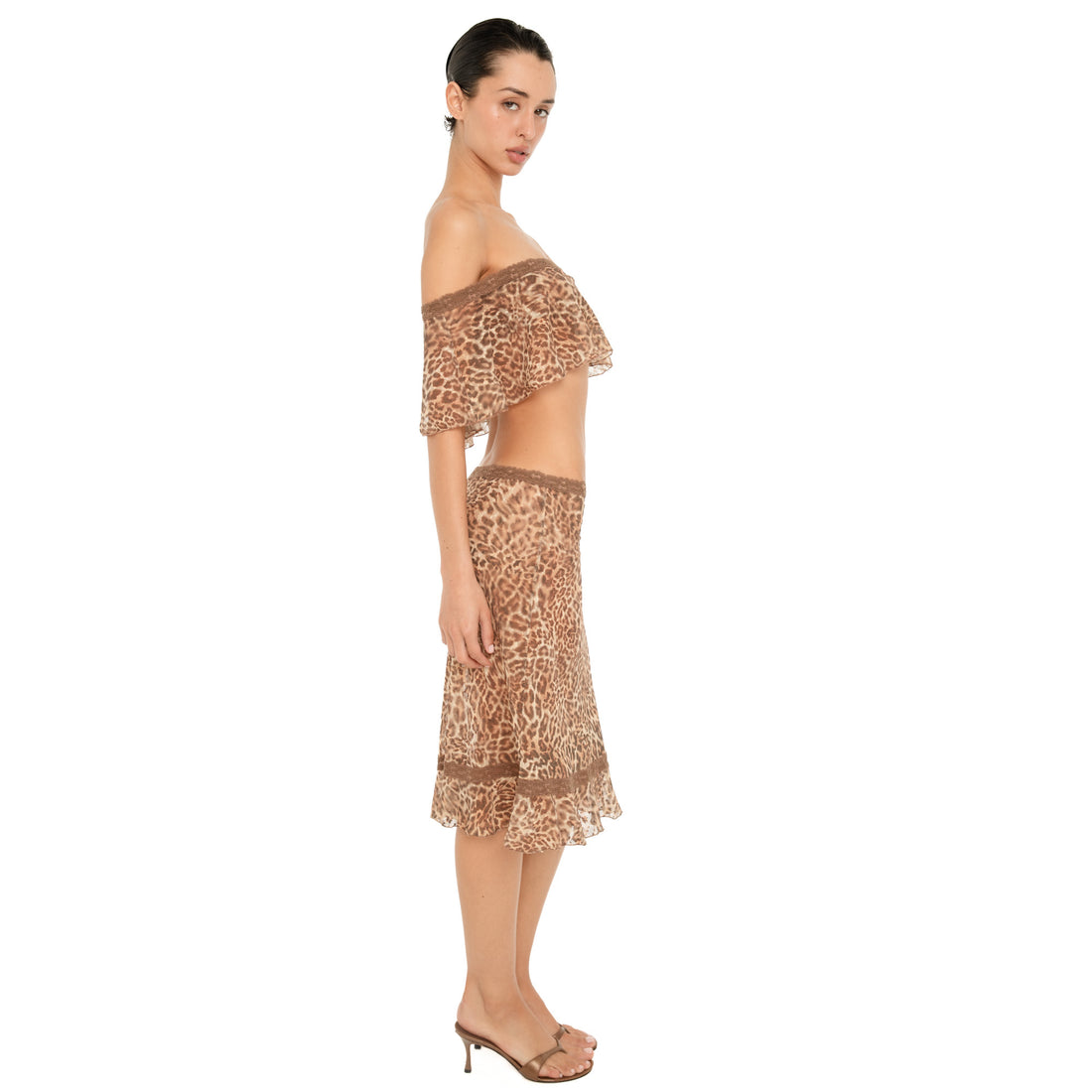 Side view of model wearing the ARE YOU AM I Liulu Skirt in leopard, showing its low rise fit, sheer fabric and ruffled hem.