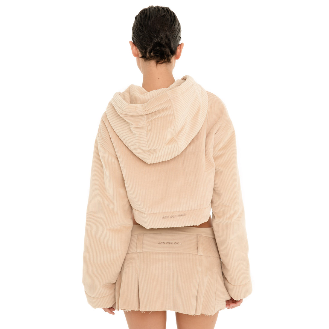 Back view of model wearing the Cahya Skirt in Sand, showing the low rise waistband, embroidered logo and pleated micro mini hem. **sand