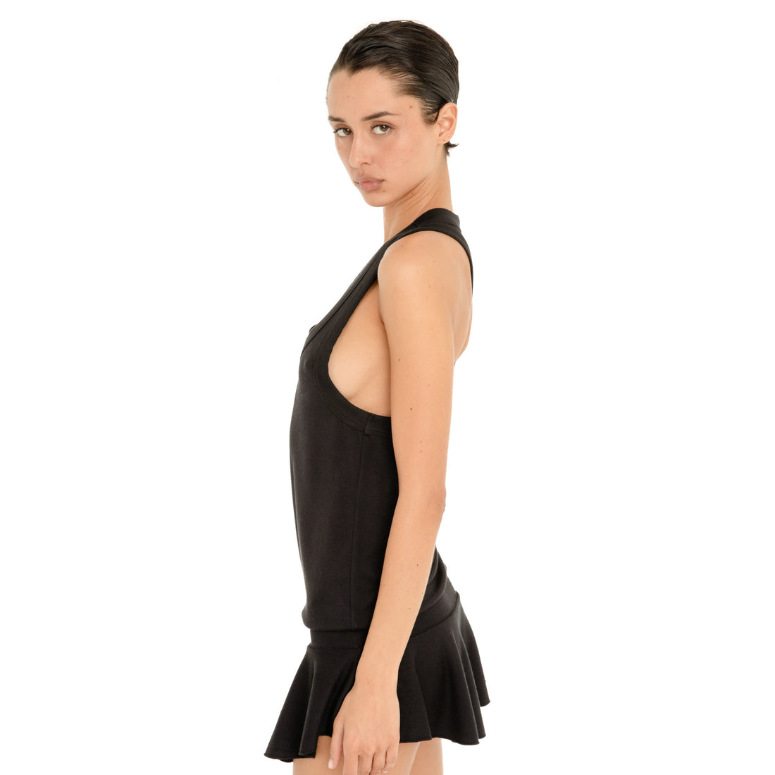 Side view of model wearing the black Suki Dress, showing the deep armholes, fitted silhouette and low flounced skirt. **black