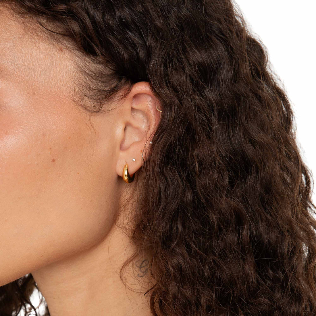 Detailed close-up of the Fala Hoops in gold worn on the model's ear, showing layering with other fine piercings.