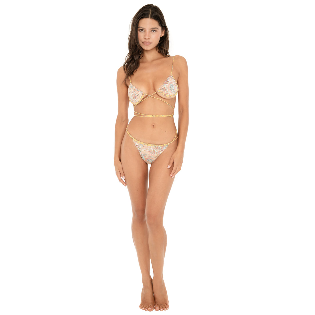 Full-length front view of a model wearing the Iti Swim Top in a pastel paisley print with the matching bikini bottom. The top features triangle cups, thin shoulder straps, and long ties crossed beneath the bust and wrapped around the waist. **paisley