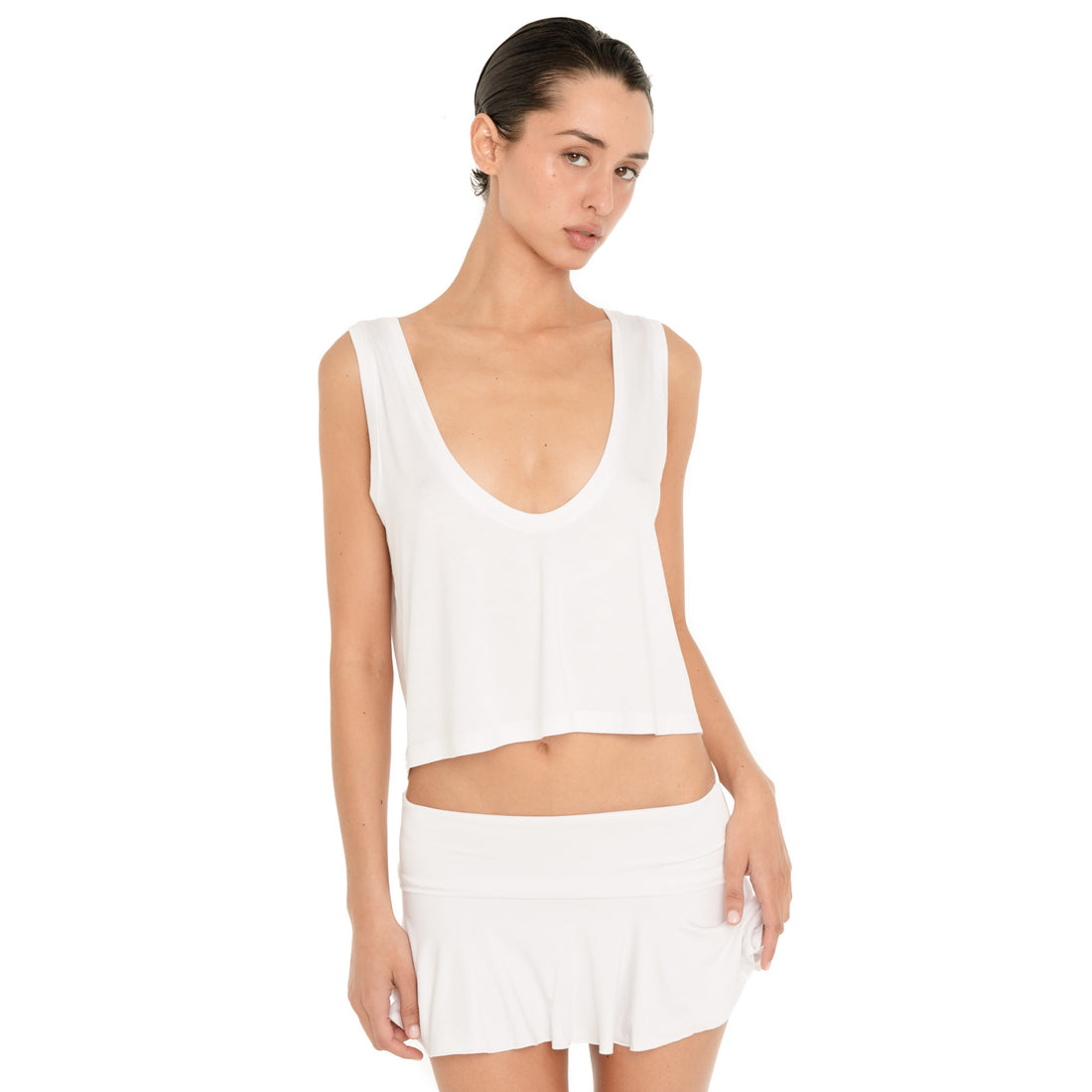 Front three-quarter view of model wearing the white Kasia Top with a white mini skirt, showing its fluid drape and cropped hem. **white
