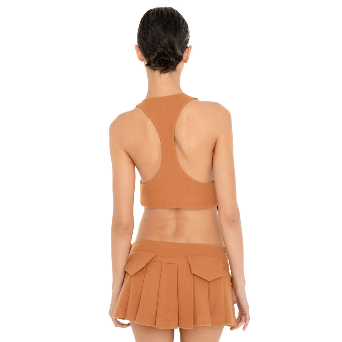 Back view of the Kess Skirt in Saffron, showing the low-rise fit, allover pleats and two flap pockets at the back waistband. **saffron