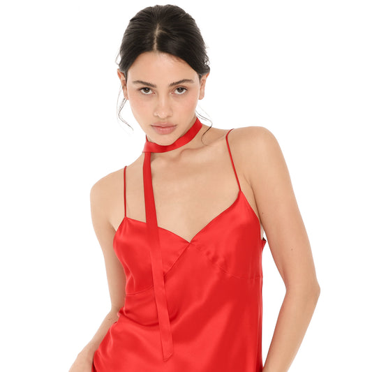 Close-up of the Nida Choker in cherry red silk, a skinny ribbon wrapped around the neck with one long tail falling across the front of a cherry red silk Eisling Dress. **cherry red