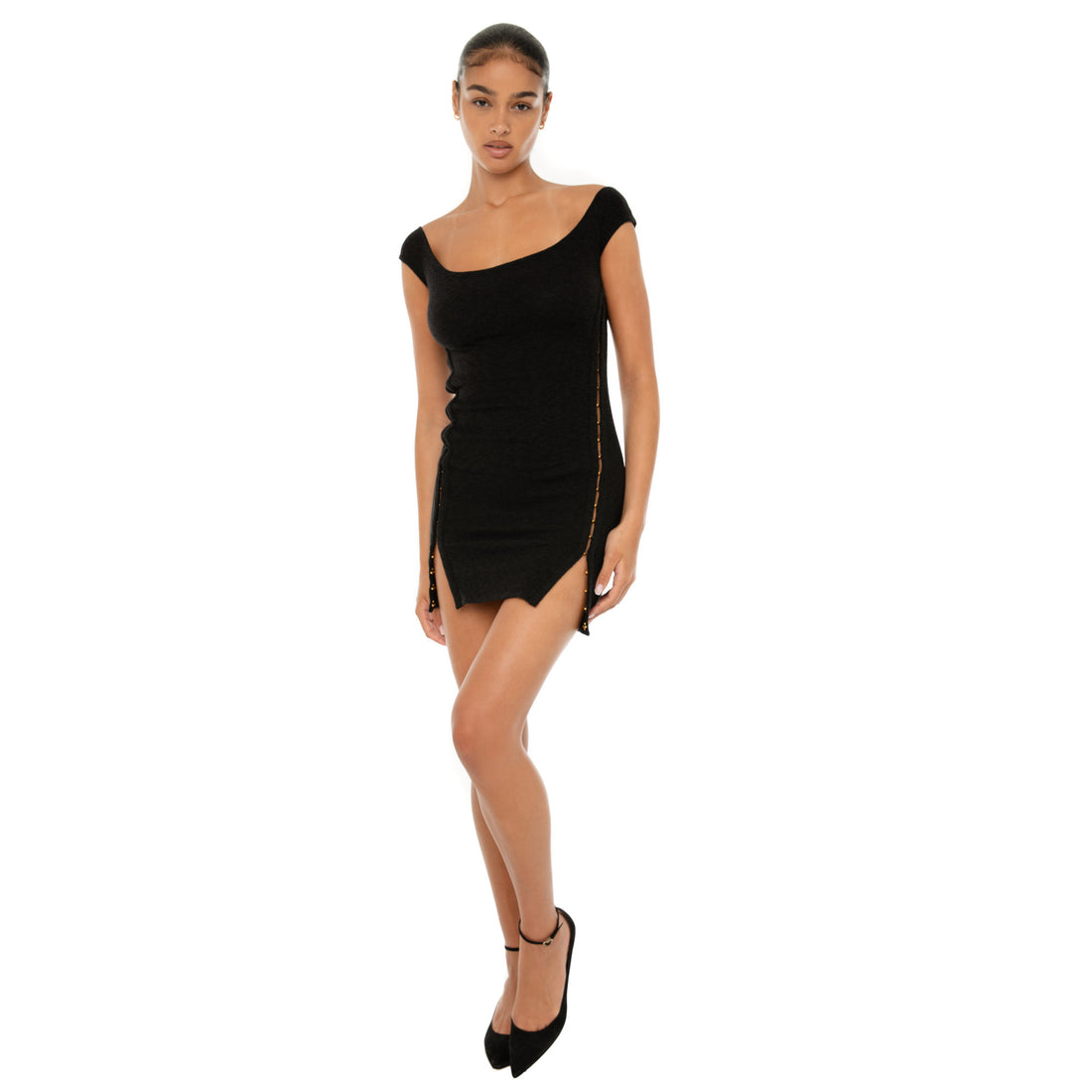 Model wearing the black Nikisa Dress — off-shoulder ribbed mini with gold hook-and-eye closures running down each side, hugging the body in a sculpted silhouette.**black