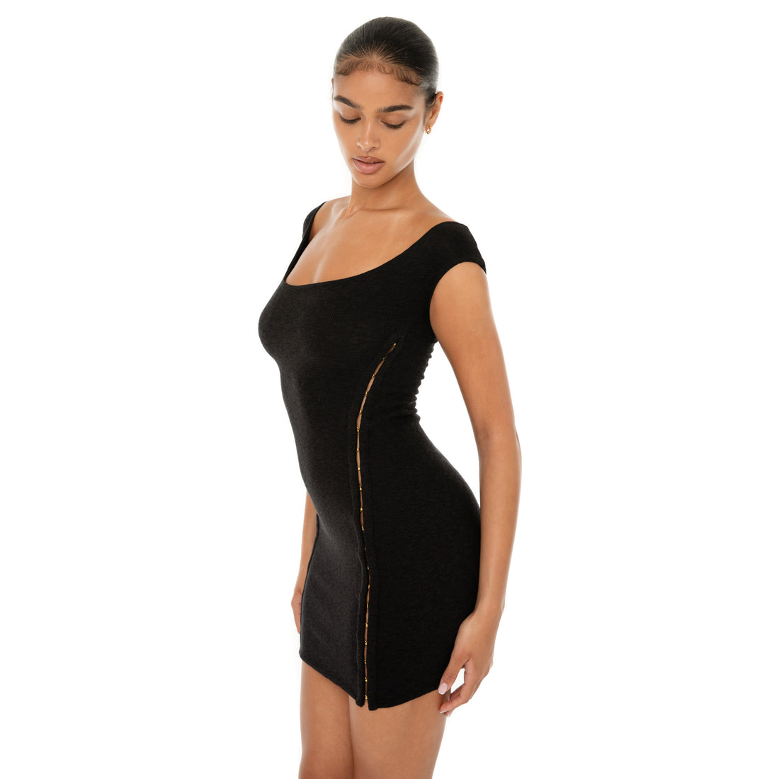 Model wearing the black Nikisa Dress — off-shoulder ribbed mini with gold hook-and-eye closures running down each side, hugging the body in a sculpted silhouette.**black