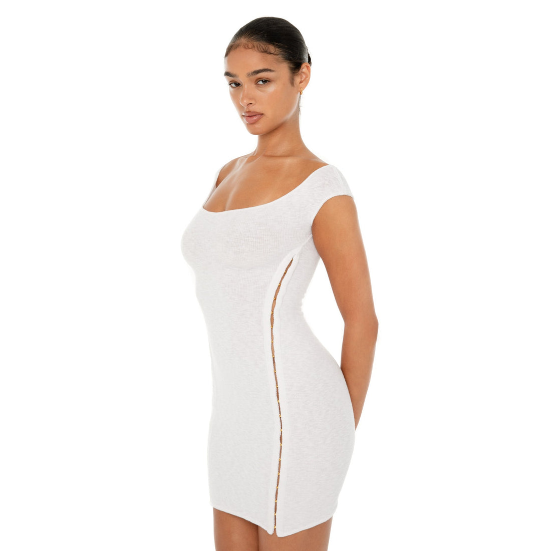 Model wearing the black Nikisa Dress — off-shoulder ribbed mini with gold hook-and-eye closures running down each side, hugging the body in a sculpted silhouette.**white