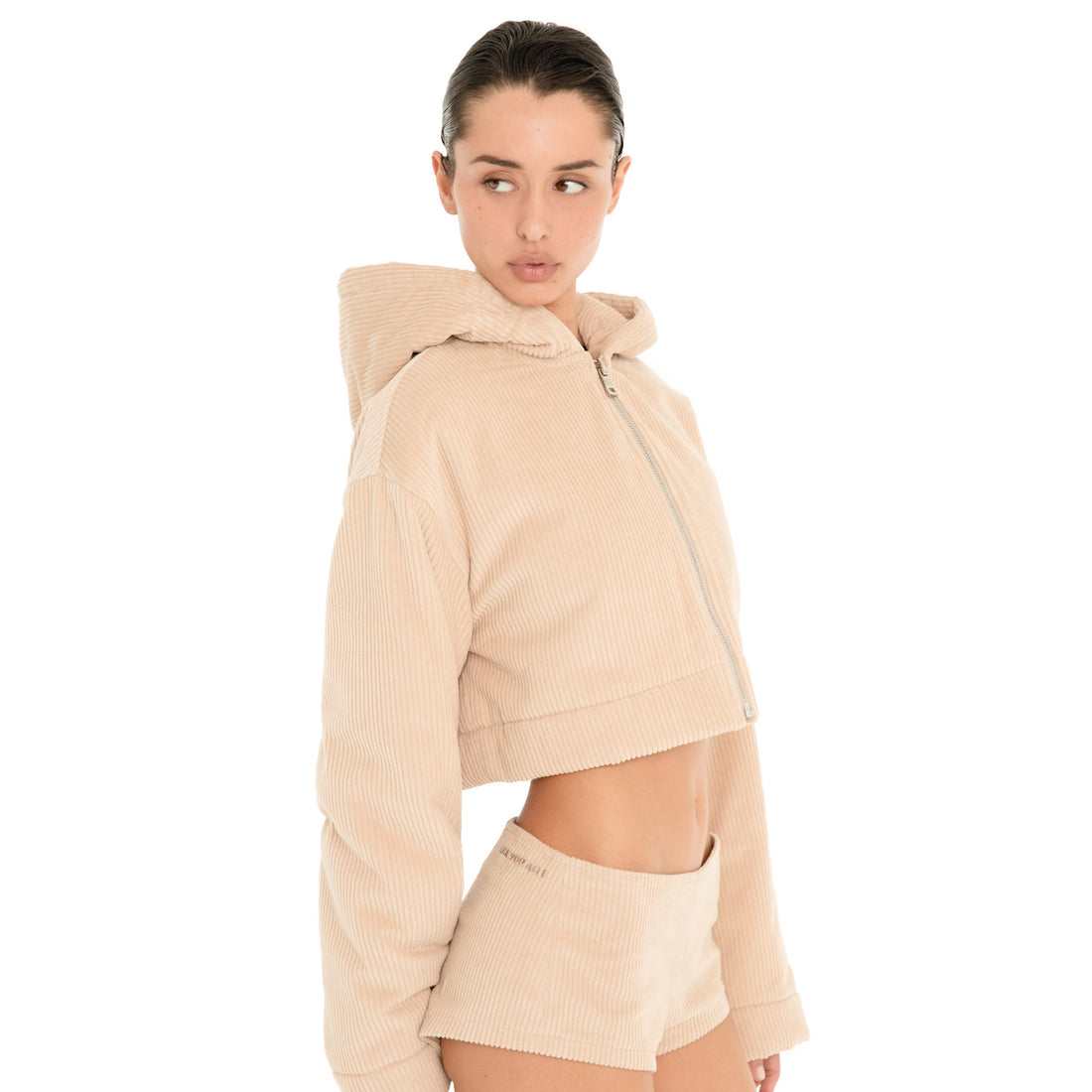 Three-quarter view of the Nimue Short in Sand, showing the low rise fit, soft ribbed texture and fitted micro silhouette with matching cropped hoodie. **sand
