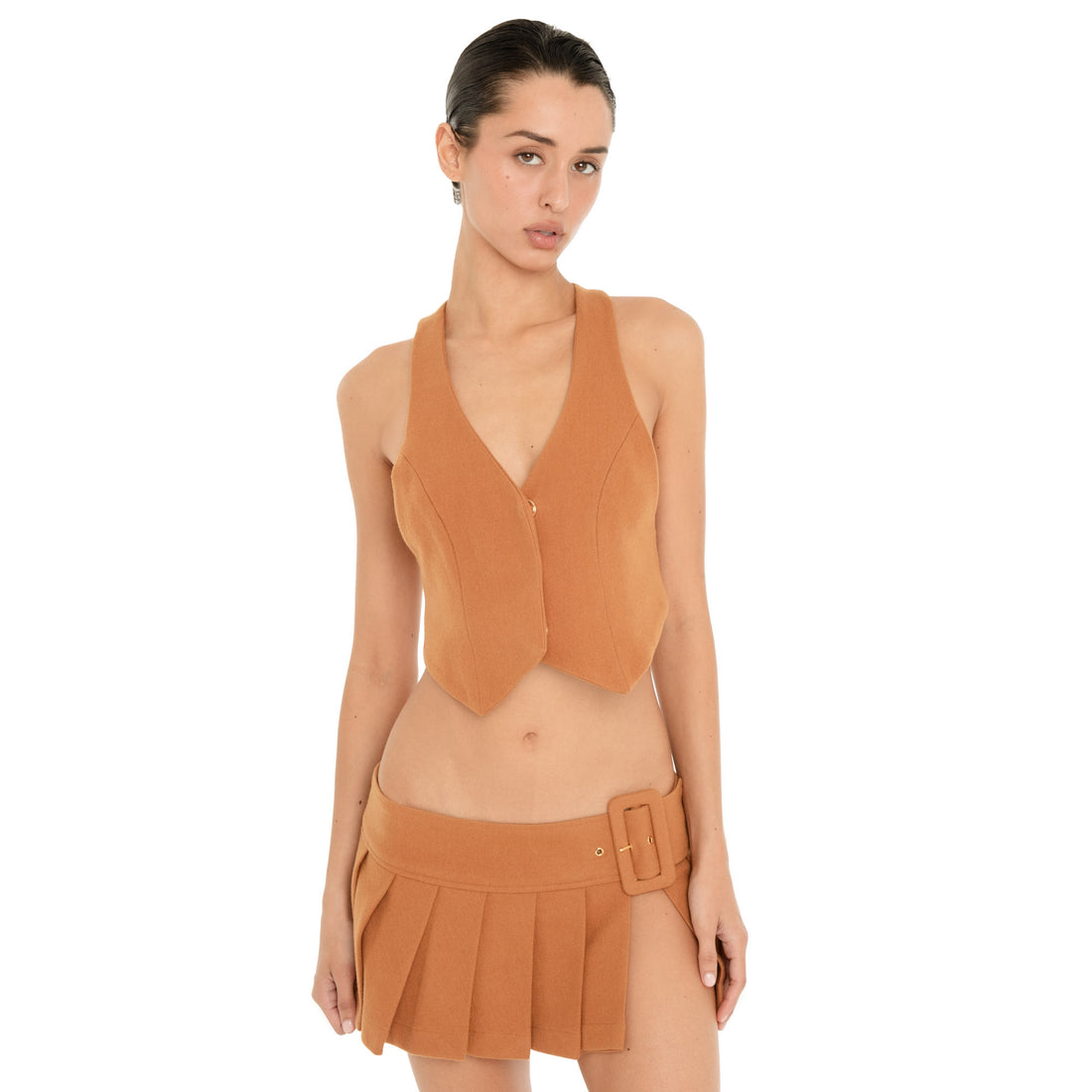 Front view of model wearing the Pau Vest in Saffron with a matching pleated mini skirt, showing the fitted waistcoat silhouette and pointed front hem. **saffron
