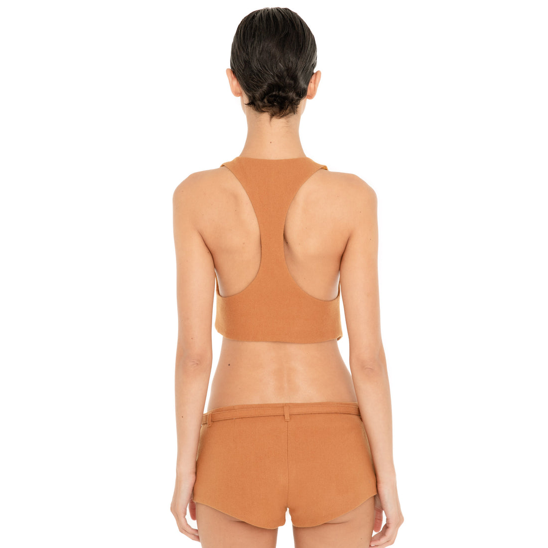 Back view of model wearing the Pika Short in Saffron, showing the low-rise waistband, belt loops, fitted silhouette and minimal back coverage. **saffron