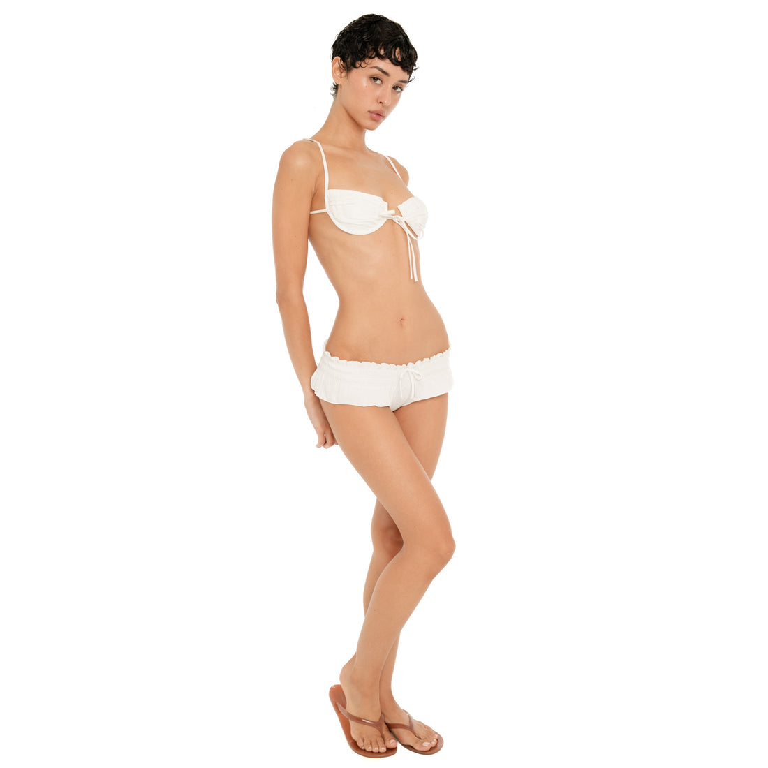 Full-length front view of model wearing the ivory Liette Boyshort low on the hips with a white ruched bra top and brown sandals.
