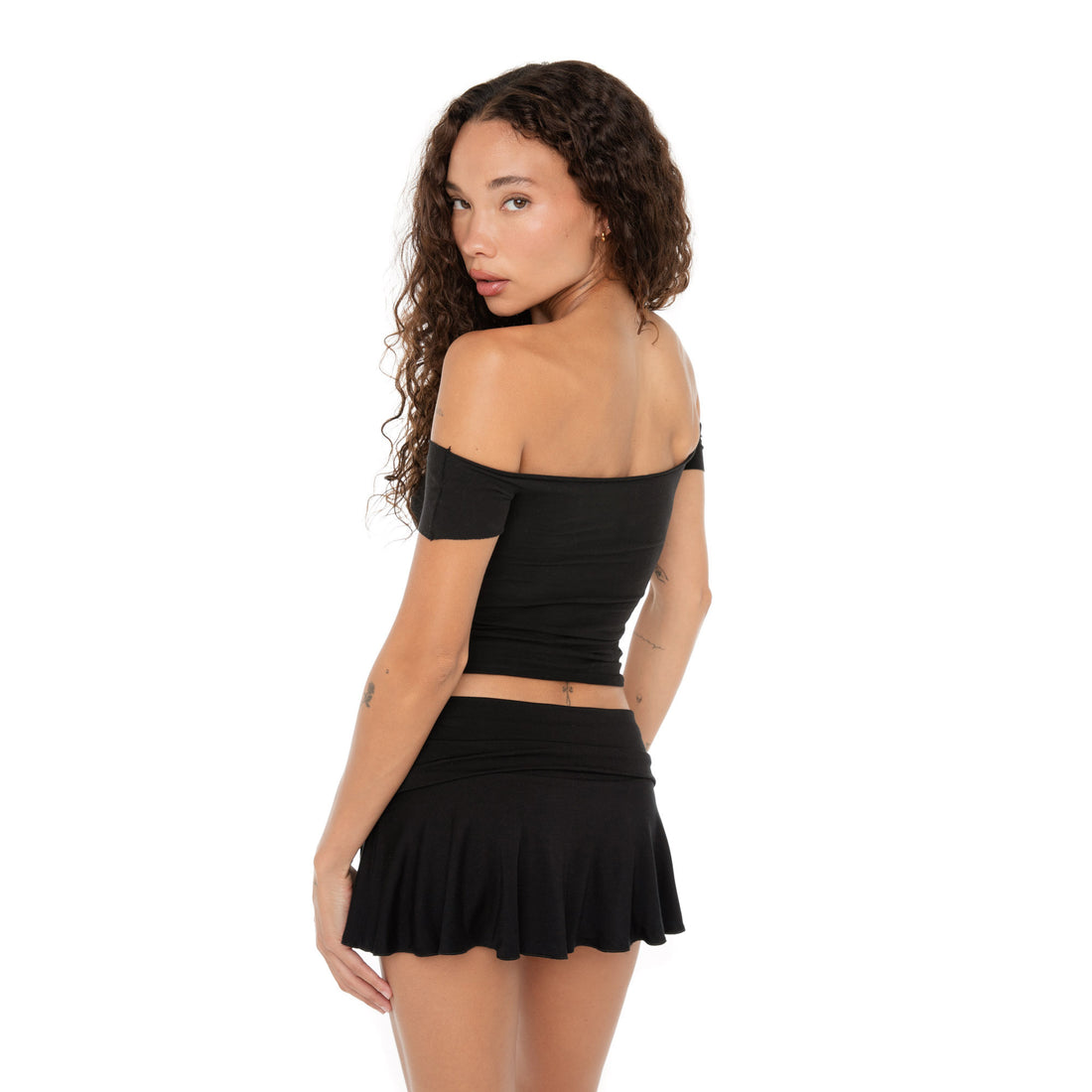 Back view of model in a black off-the-shoulder top and flared mini skirt, looking over her shoulder. **black
