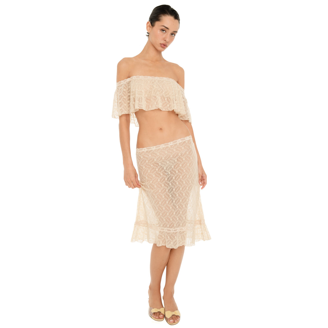 Model wearing the Liulu skirt in nude, a sheer lace midi skirt with a low rise waist, delicate lace trim, and ruffled hem, styled with the matching off shoulder top. **nude