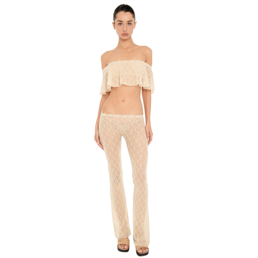 Front view of model wearing the Liani Pant in Nude, a sheer floral lace pant with a low rise lace-trimmed waistband and flared leg. **nude