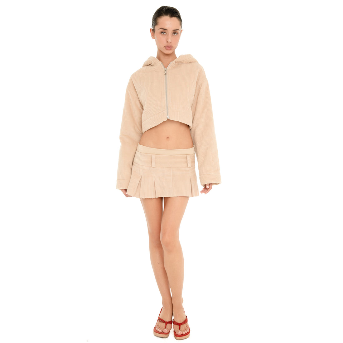 Full-length front view of model wearing the Cahya Skirt in Sand, a low rise corduroy micro mini skirt with a wide waistband, belt loops and pleated hem.**sand