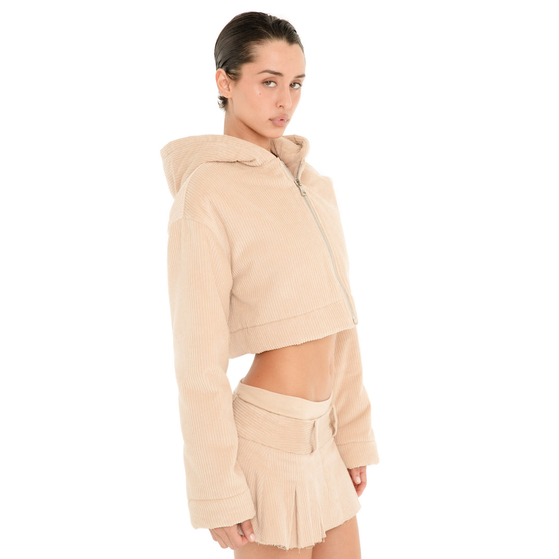 Three-quarter view of model wearing the Cahya Skirt in Sand, showing the low rise fit, wide waistband, belt loops and pleated mini silhouette. **sand