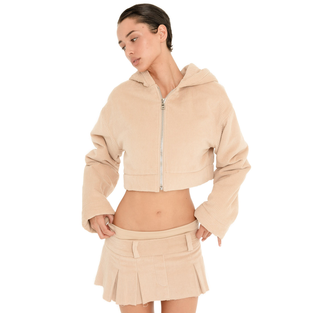 Three-quarter front view of model wearing the Cahya Skirt in Sand, highlighting the low rise fit, wide waistband and pleated micro mini silhouette. **sand