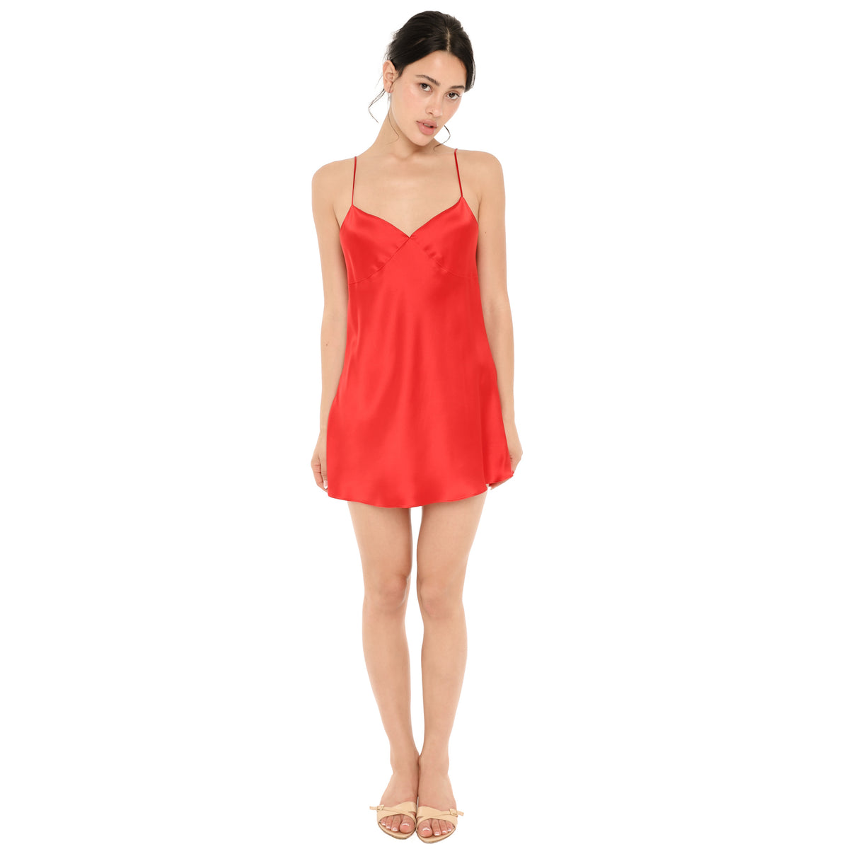 Model wearing the Eisling Dress in cherry red silk, a mini slip dress with a V neckline, seamed bust and thin straps, shown from the front with nude sandals. **cherry red