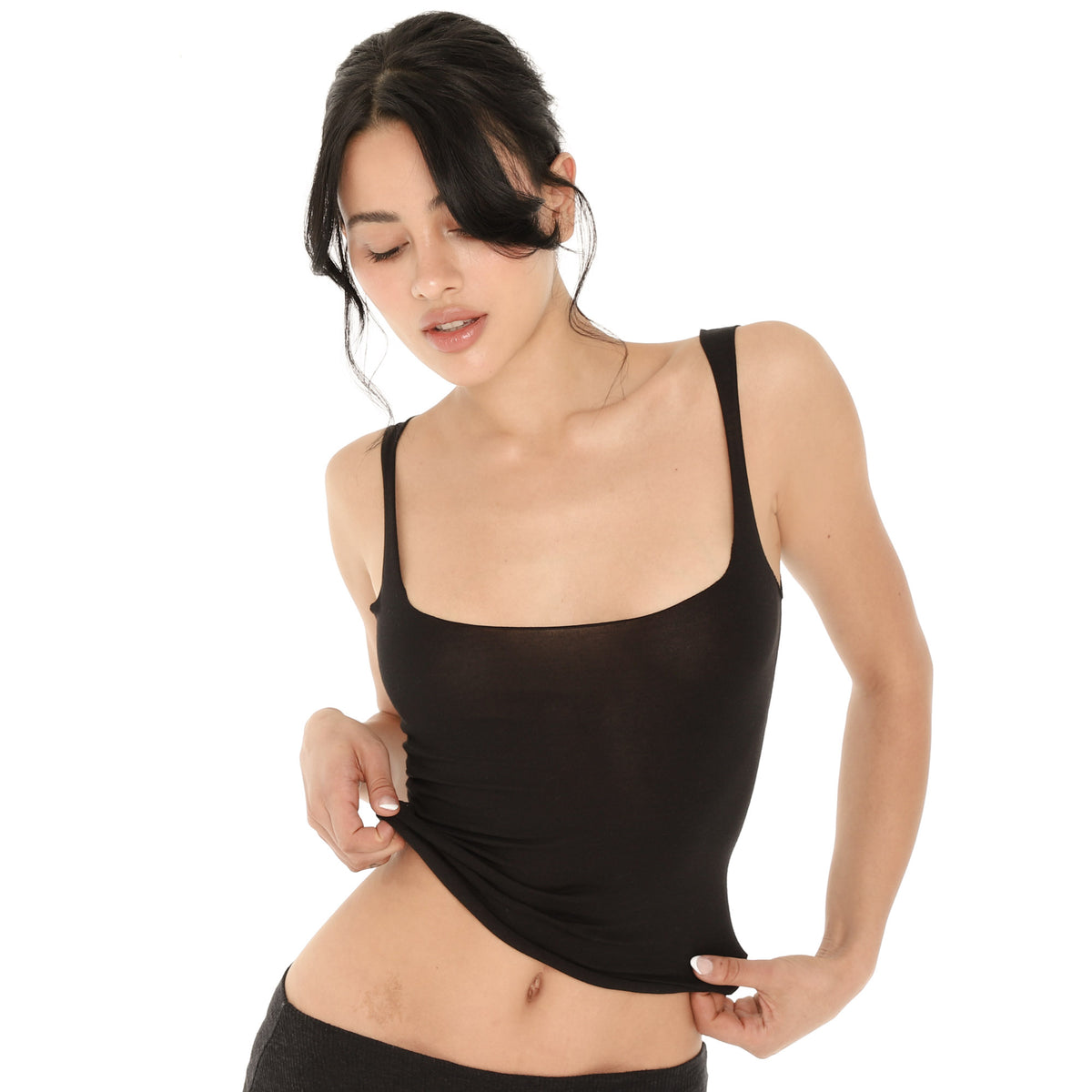 Model lifting the hem of the black Elix Tank to show the stretchy, sheer knit fabric and the rolled raw edge **black