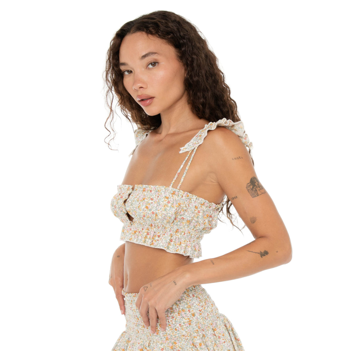 Side angle of model in the Are You Am I Eran Top floral crop top, showing the smocked fit, button front, and ruffle strap detail. **floral