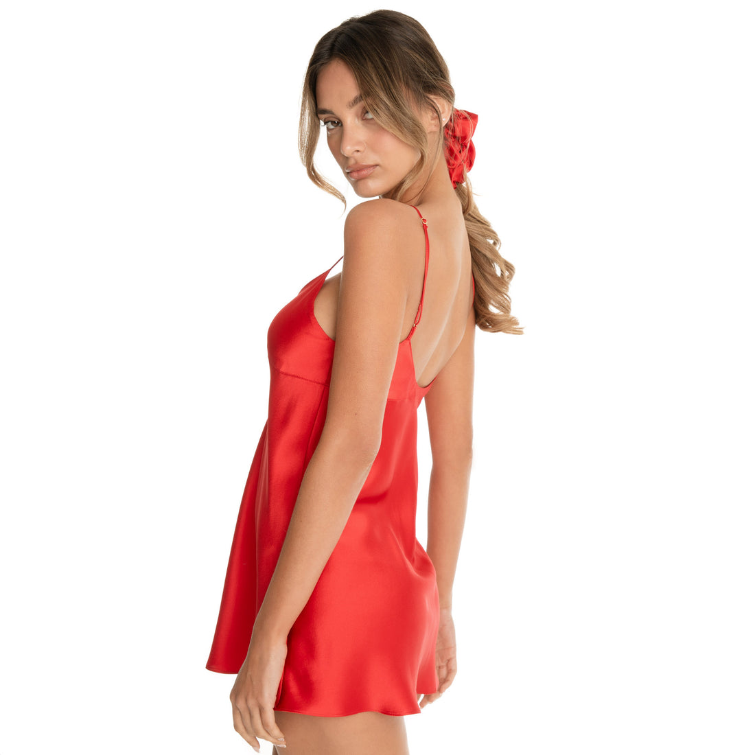 Side angled view of a model wearing an oversized silk scrunchie with a low ponytail, showing the soft, plush silhouette and reflective silk finish **cherry-red