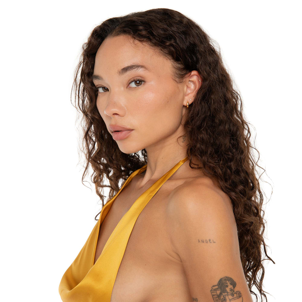 Side view of the model wearing the Fala Hoops in gold, paired with a mustard silk halter top and loose curls.