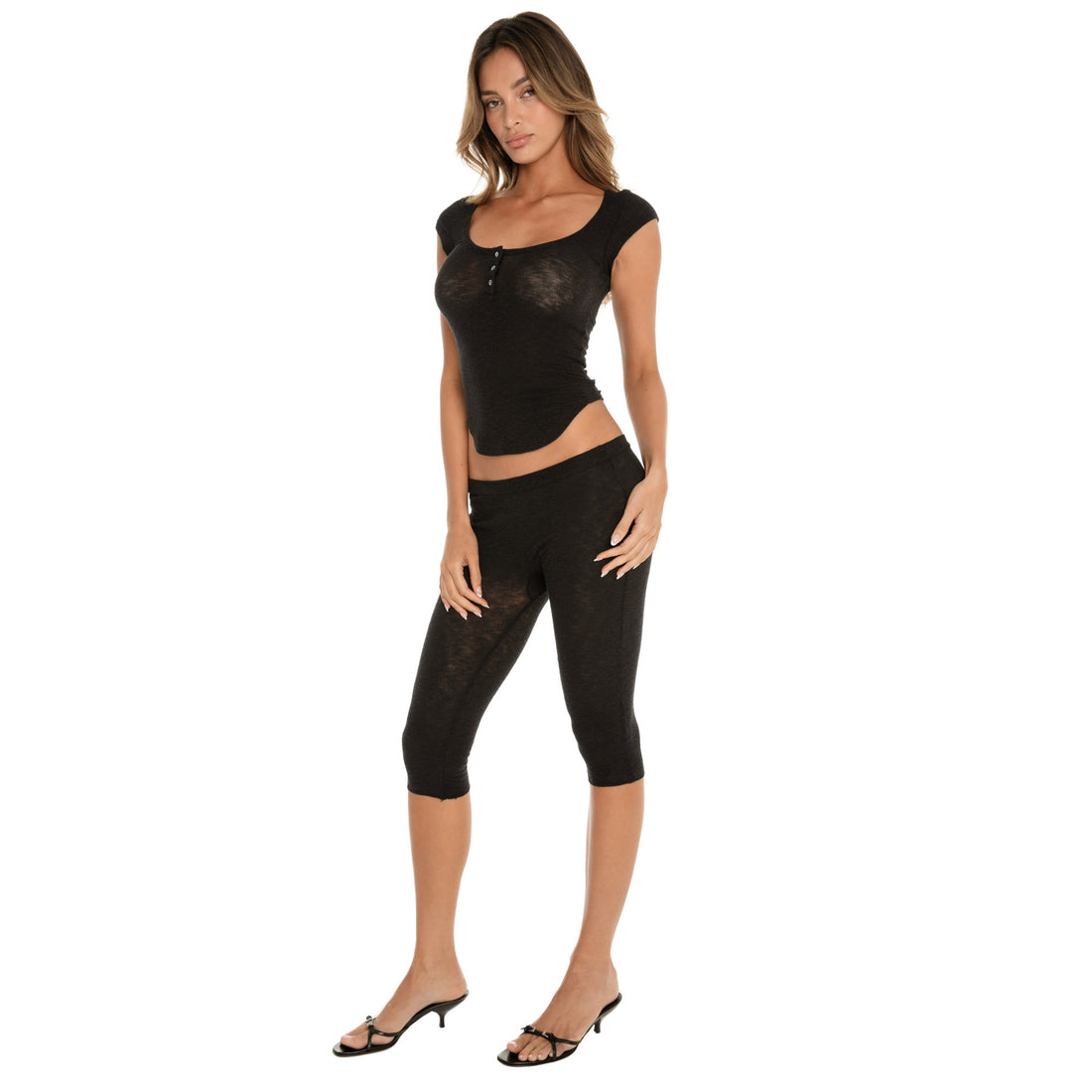 Three-quarter front view of a fitted cap sleeve henley top and capri leggings, emphasizing the contoured silhouette, scoop neckline, and soft semi-sheer texture **black