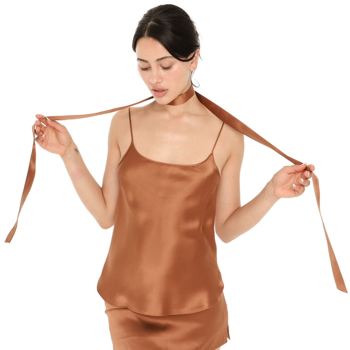 Model holding both ends of the copper silk Isolde Scarf out to the sides to show its length, with the scarf wrapped around her neck, worn with a matching copper silk cami and the Tini Skirt **copper