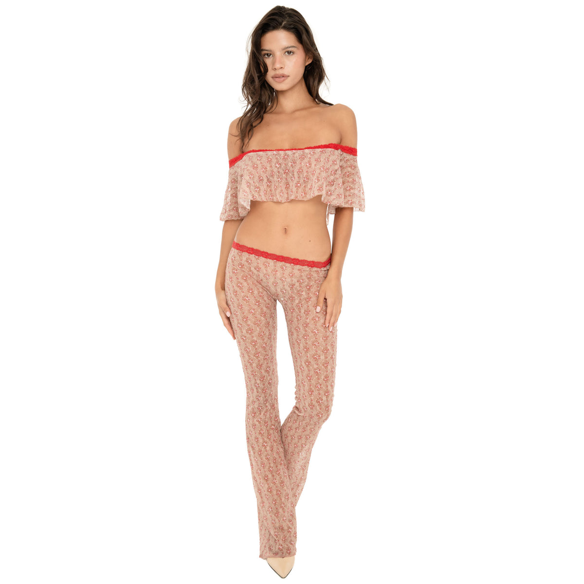 Model wearing the Liani Pant in Cherry Blossom, a sheer floral lace low-rise pant with a slim flared leg and red lace-trim waistband, styled with a matching off-the-shoulder top **cherry blossom