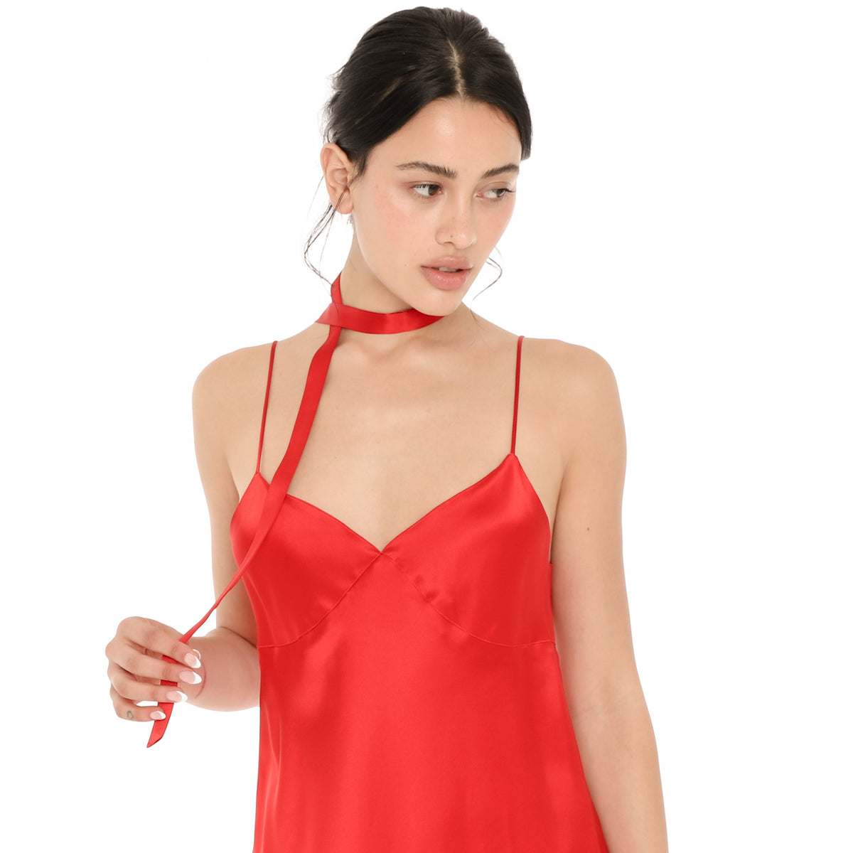 Model holding the end of the cherry red silk Nida Choker, a skinny ribbon wrapped around the neck, worn with a cherry red silk Eisling Dress. **cherry red