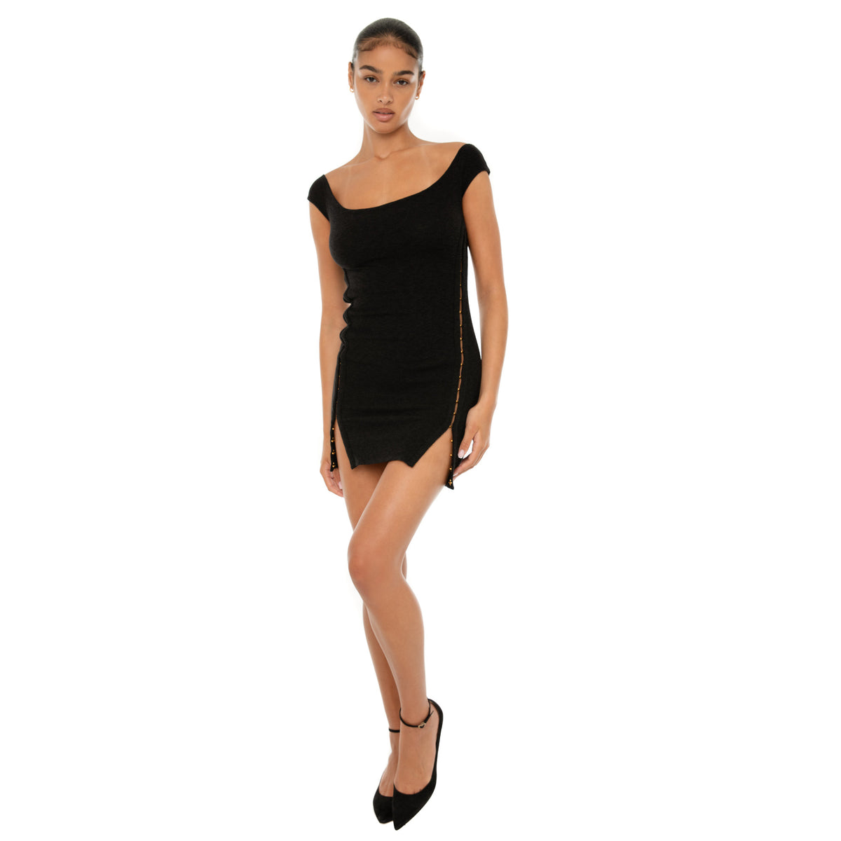 Model wearing the black Nikisa Dress — off-shoulder ribbed mini with gold hook-and-eye closures running down each side, hugging the body in a sculpted silhouette.**black