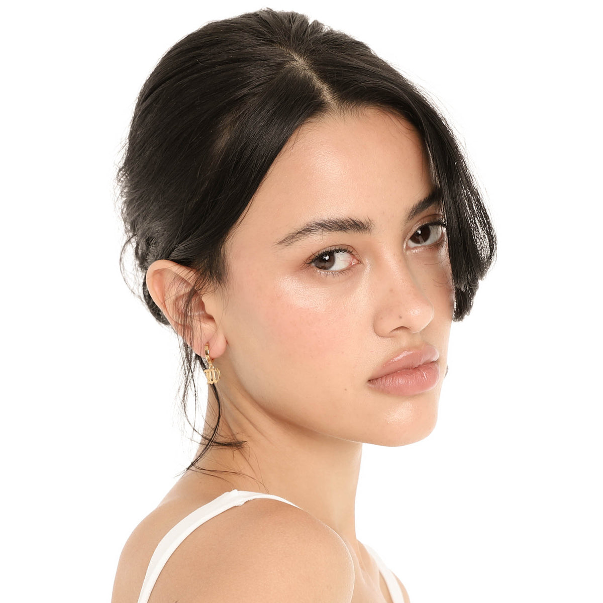 Close three-quarter view of the Nimi Earring in W, showing the gold huggie hoop and the old English letter W charm hanging just below the earlobe