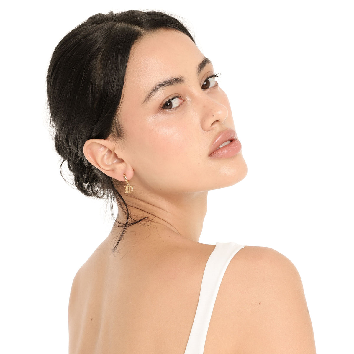 Model looking over her shoulder in the Nimi Earring in W, showing the small gold hoop and gothic letter W charm against her neck