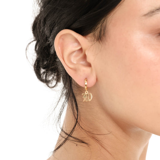 Close-up of the Nimi Earring in W on the ear, showing the polished gold huggie hoop and the detailed cutout of the old English letter W charm