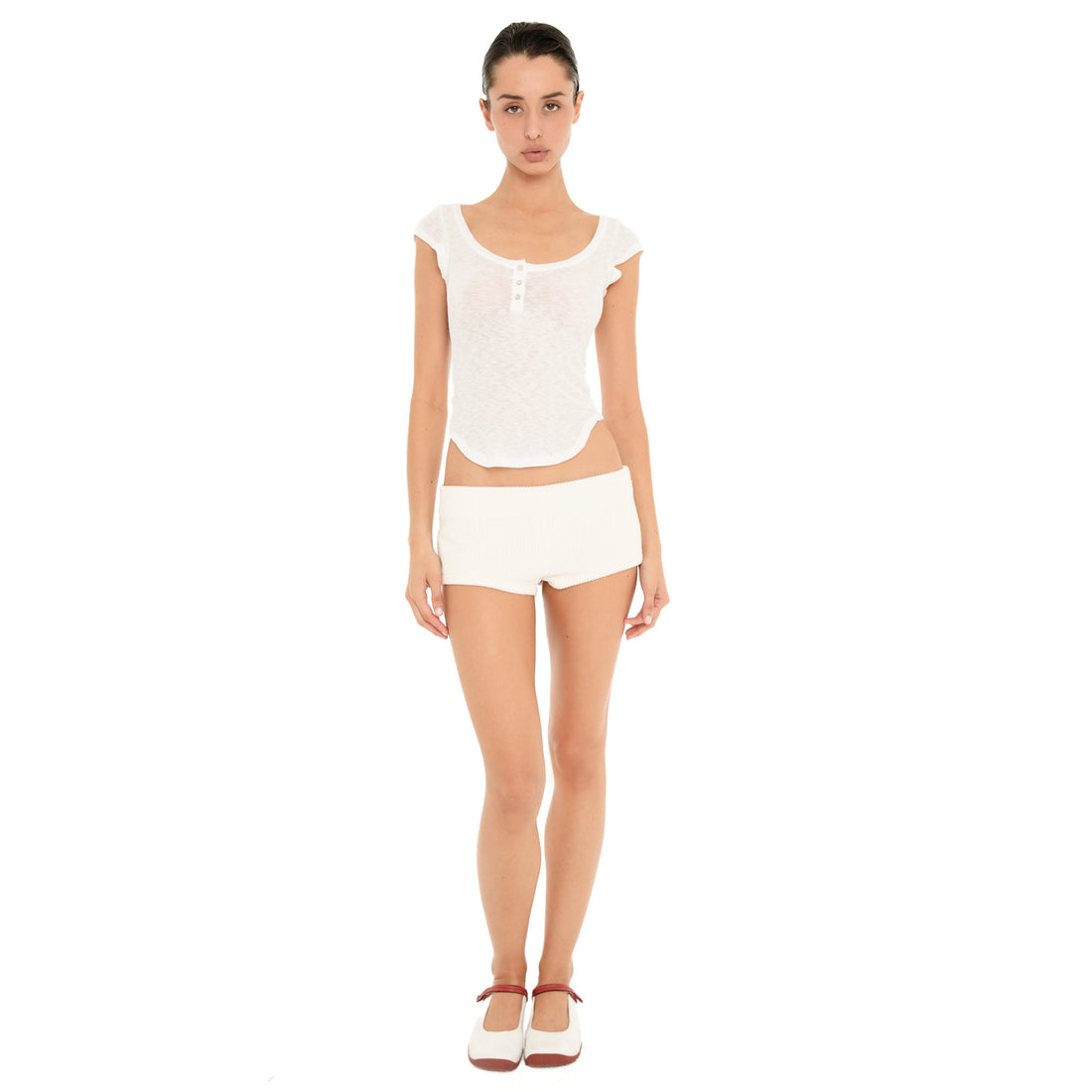 Front full-length view of model wearing the ivory Nimue Short, a low-rise fitted micro short in soft ribbed fabric, styled with a white henley top. **ivory