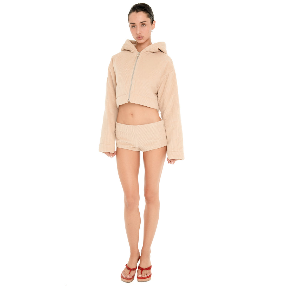 Full-length front view of model wearing the Nimue Short in Sand, a low rise ribbed micro short, styled with a matching cropped zip-up hoodie. **sand