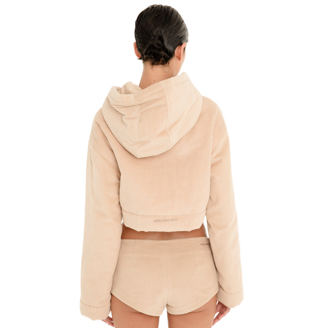 Back view of model wearing the Nimue Short in Sand, showing the low rise waistband, curved short hem and embroidered Are You Am I logo. **sand