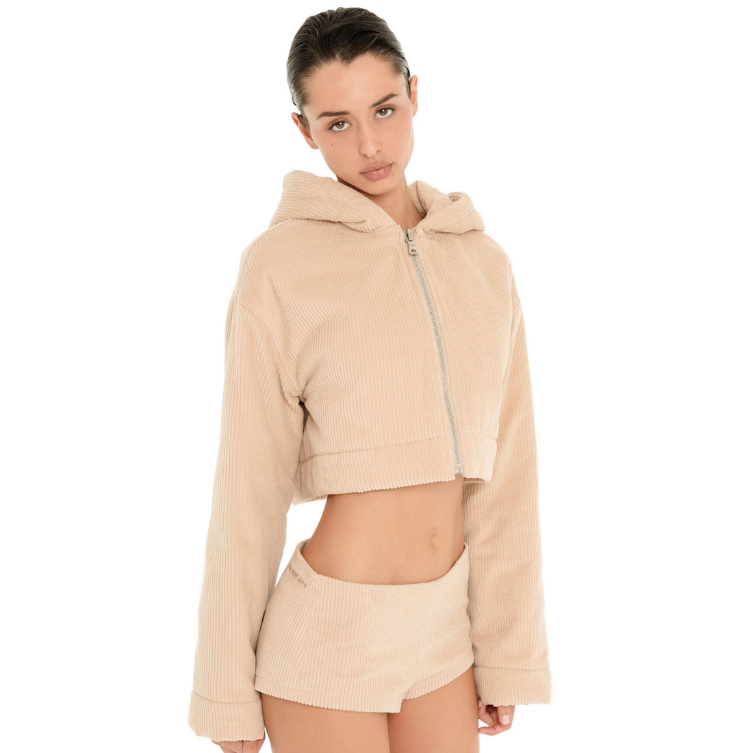 Front three-quarter view of model wearing the Nimue Short in Sand with a matching cropped hoodie, showing the low rise waist and fitted micro length. **sand