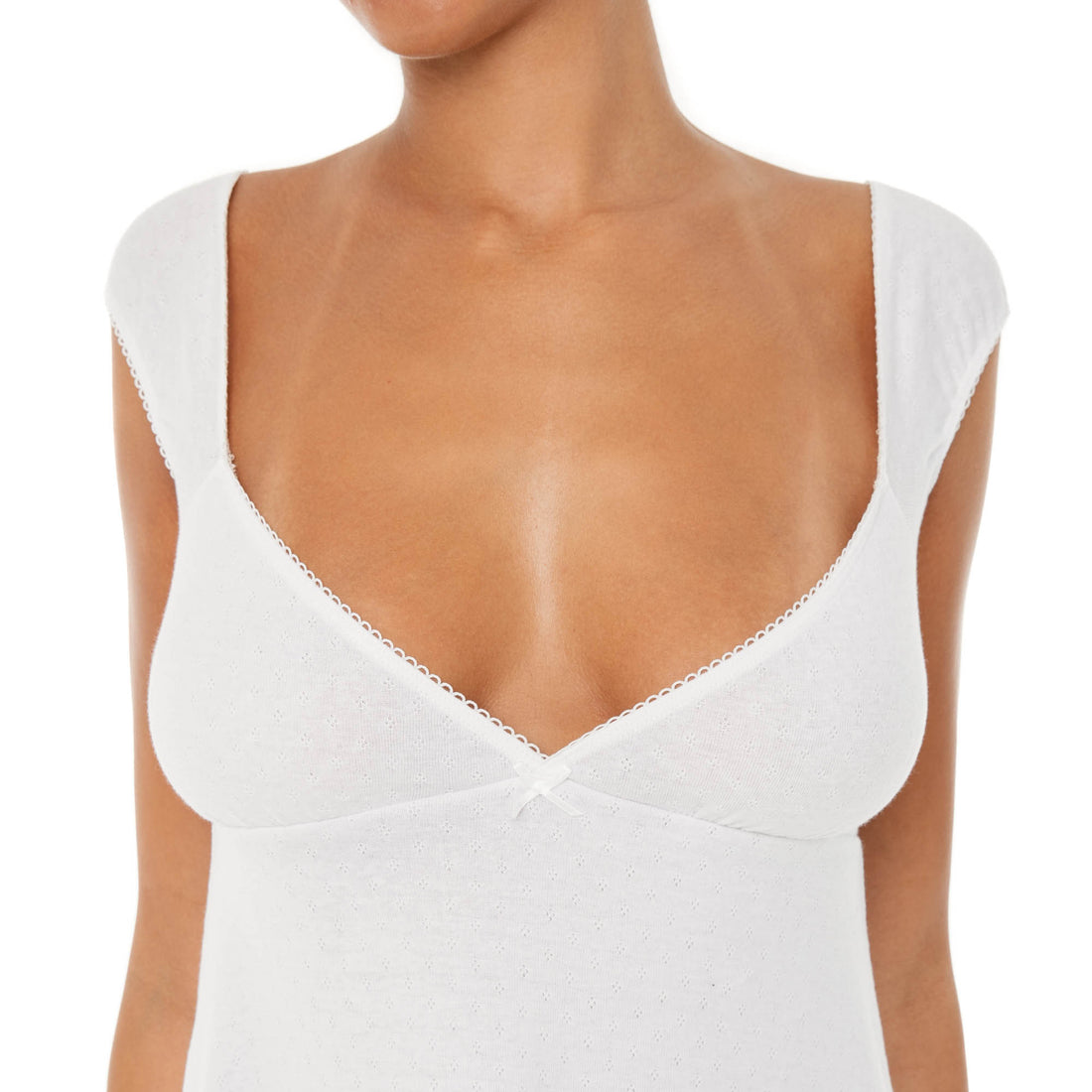 Model wearing the Eveli Dress — white cotton mini with cap sleeves and deep scoop neckline, finished with delicate scalloped trim and subtle sheer texture.