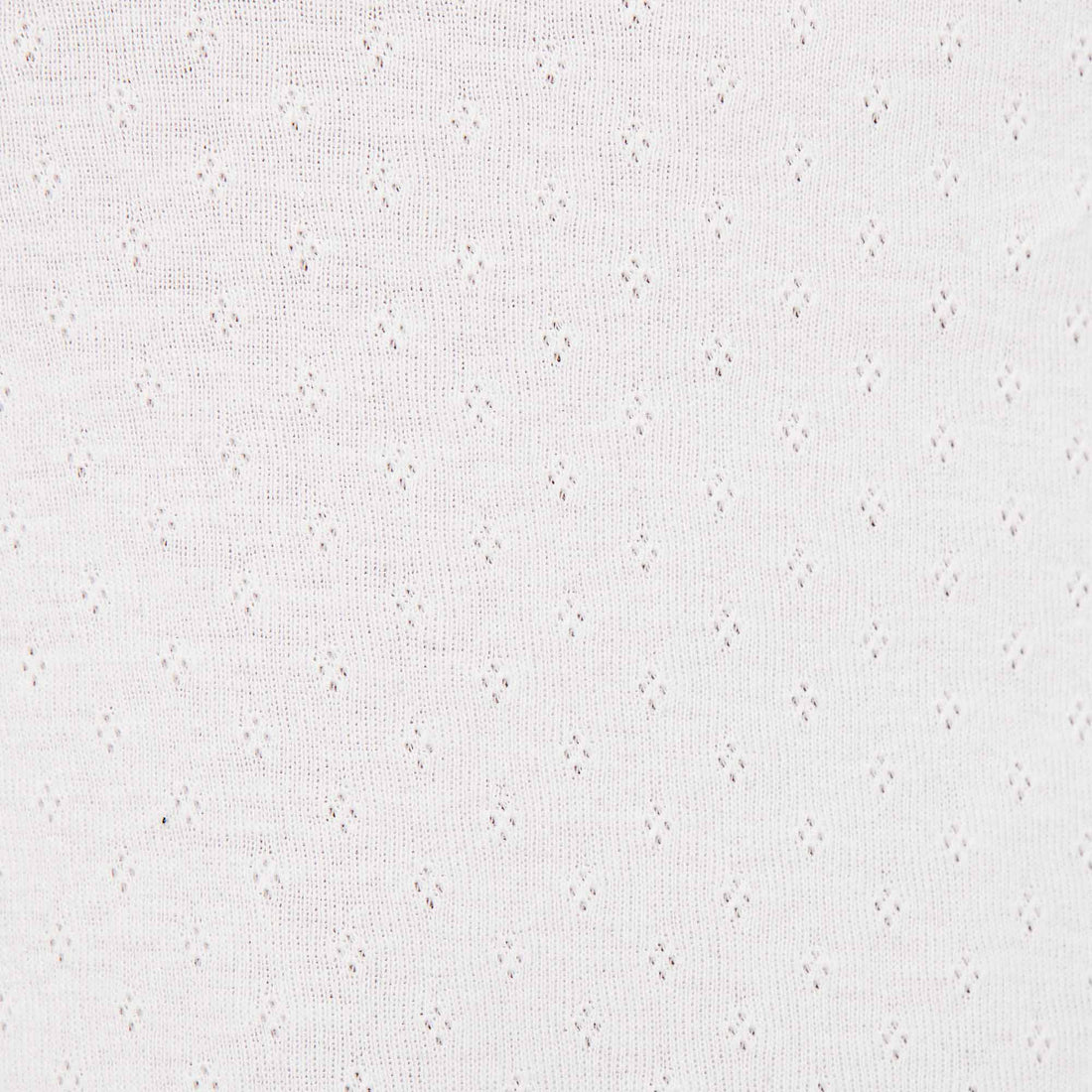 Model wearing the Eveli Dress — white cotton mini with cap sleeves and deep scoop neckline, finished with delicate scalloped trim and subtle sheer texture.