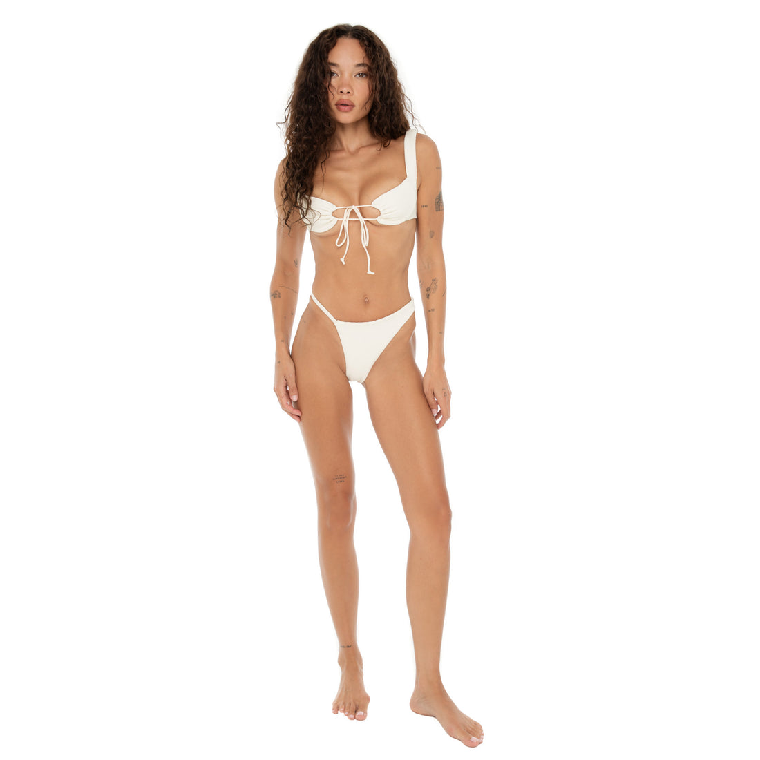 Model wearing the Are You Am I Seren Swim Bottom in Cream, a high-cut bikini bottom with asymmetrical silhouette, paired with matching swim top. **cream