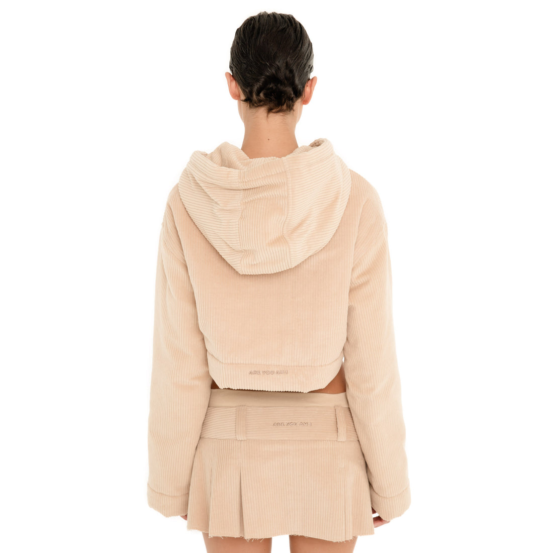 Back view of model wearing the Sfera Jacket in Sand, showing the oversized hood, relaxed long sleeves, cropped silhouette and embroidered logo at the hem. **sand