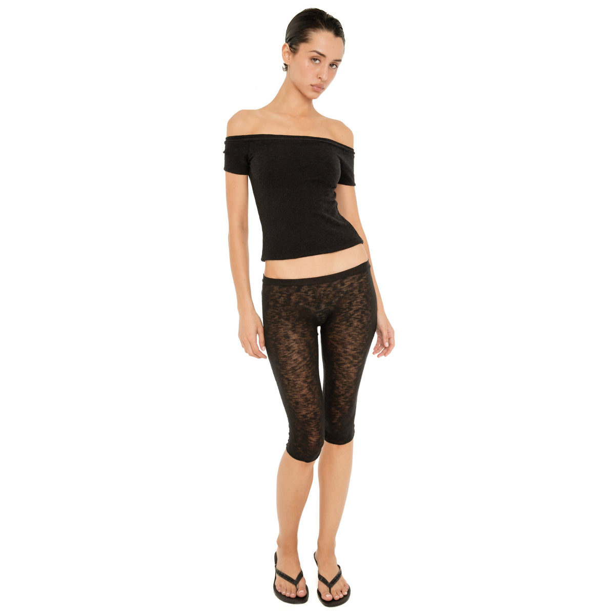 Model wearing the black Solei off-the-shoulder top with sheer black cropped pants and flip-flops **black