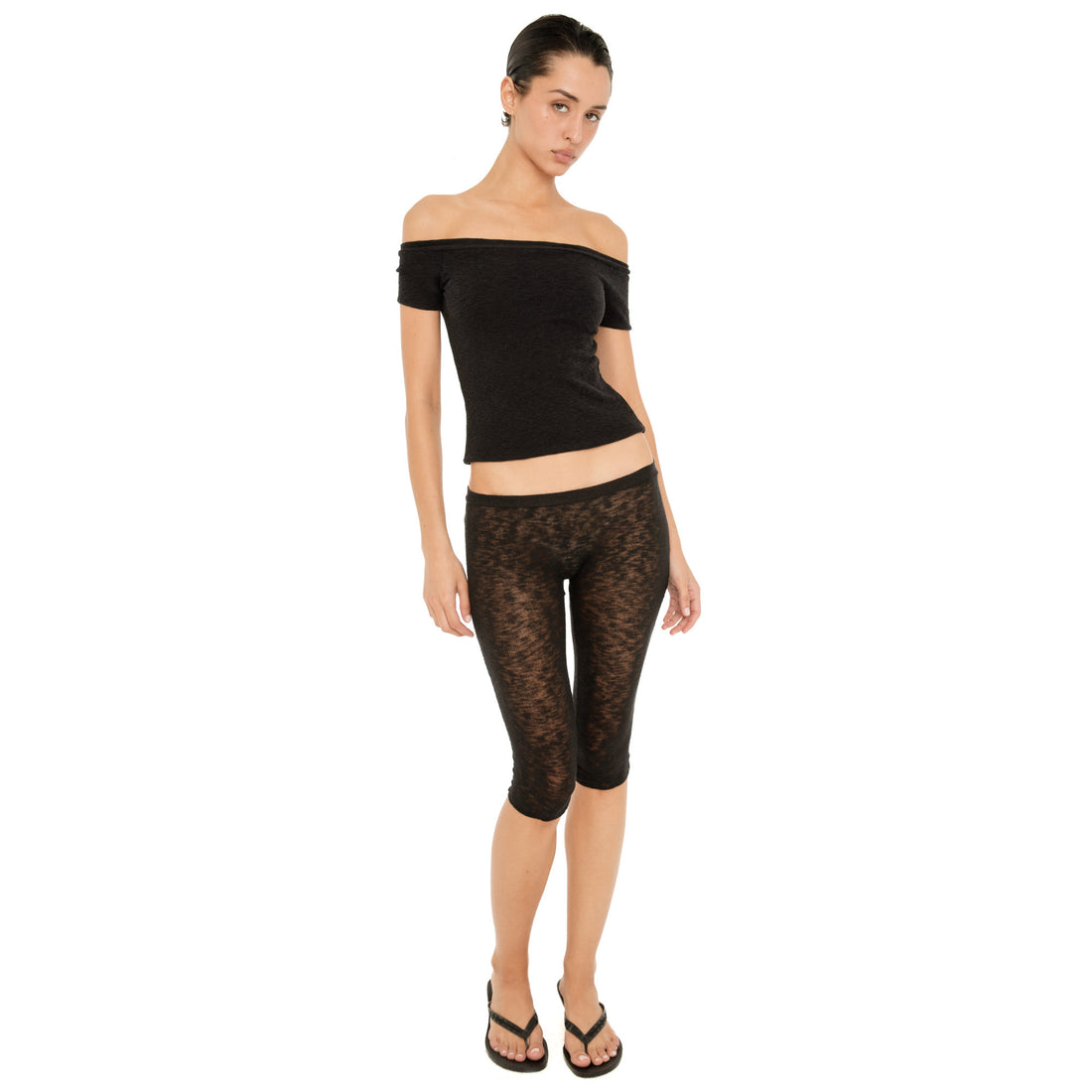 Model wearing the black Solei off-the-shoulder top with sheer black cropped pants and flip-flops **black