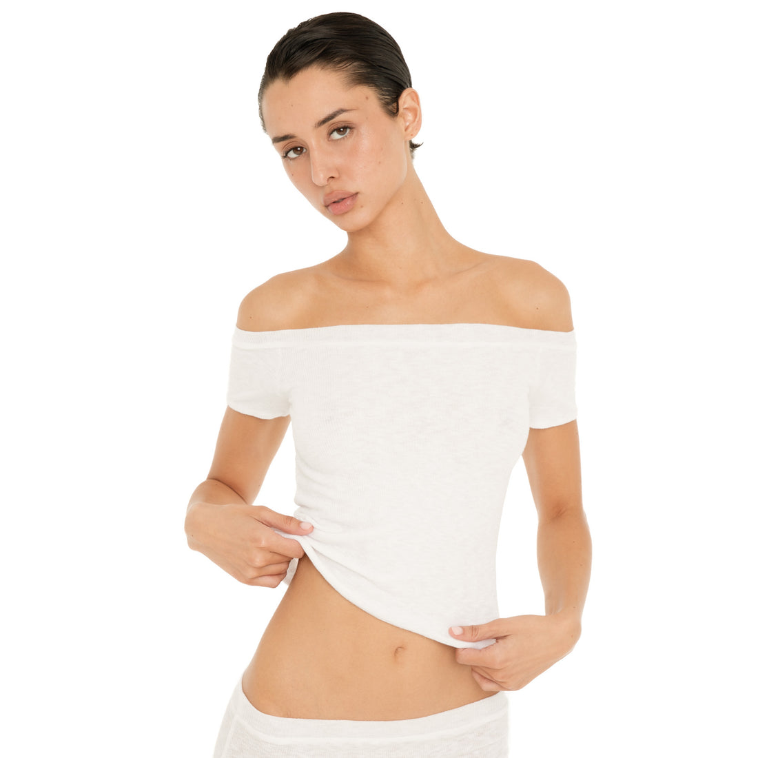 Front view of the white Solei off-the-shoulder top as the model lifts the hem to show the lightweight fabric and fit **white
