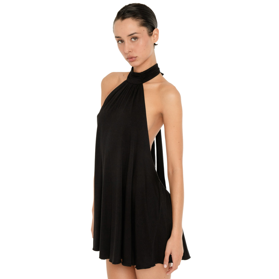 Three quarter front view of the black halter mini dress, showing the wrapped high neckline, sleeveless design, low cut sides, and fluid draped silhouette. **black