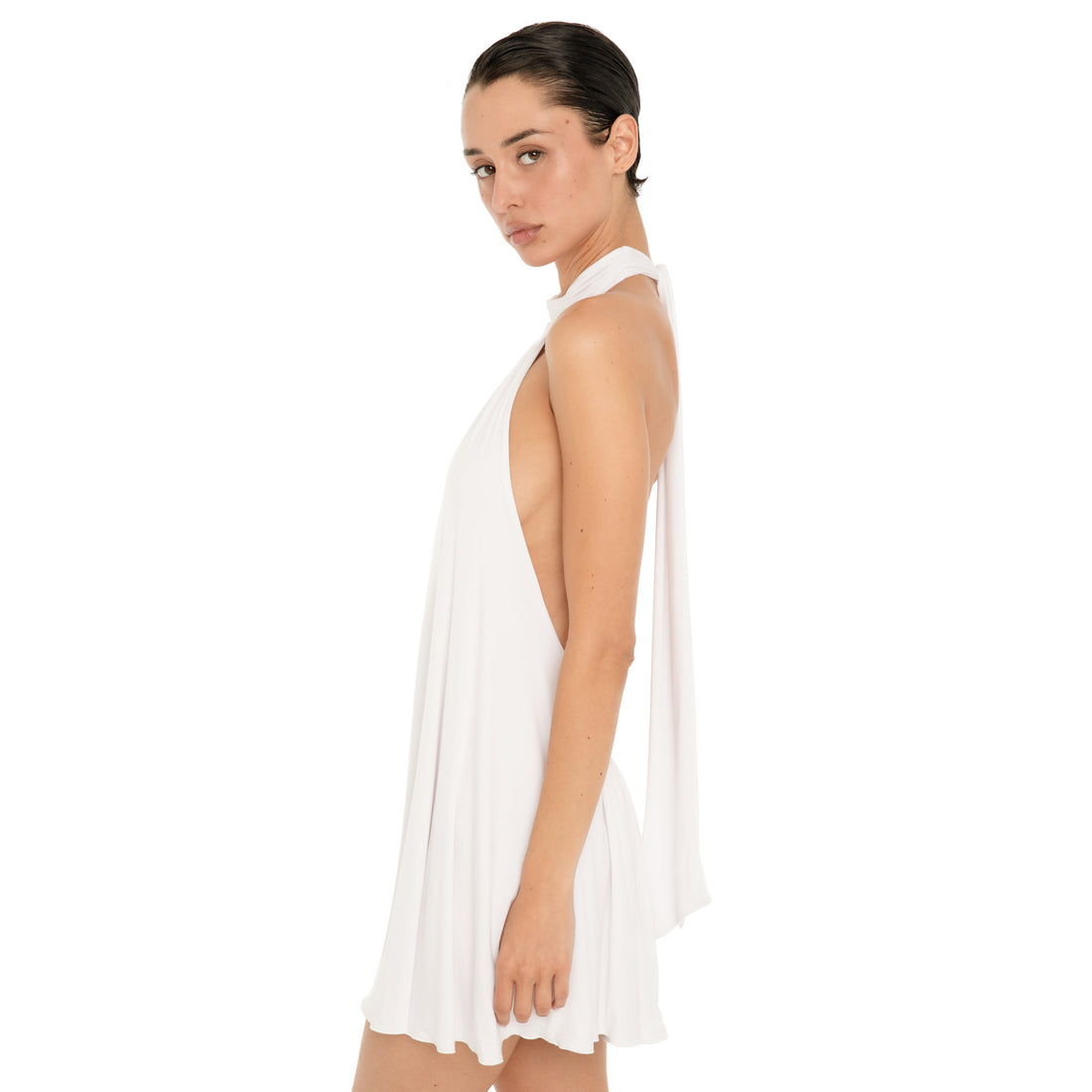 Side view of the white halter mini dress, showing the high neckline, low cut side, fluid draping, and relaxed mini length silhouette. **white