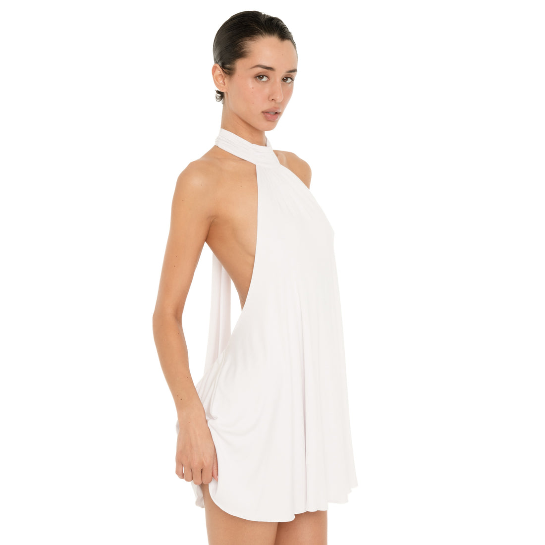 Three quarter back view of the white halter mini dress, highlighting the open back, long neck ties, low gathered waist, and fluid mini skirt. **white